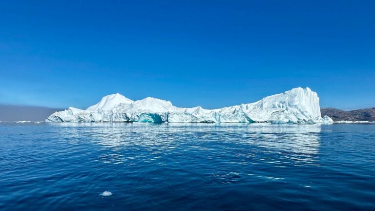 Capture of icebergs in Greenland with clear skies and ocean reflections, illustrating breathtaking Arctic beauty.